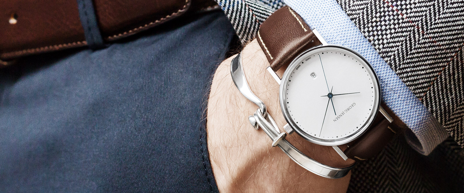 On model photo of Georg Jensen Koppel collection quartz Swiss made watch with brown calfskin strap and mens Torun bangle
