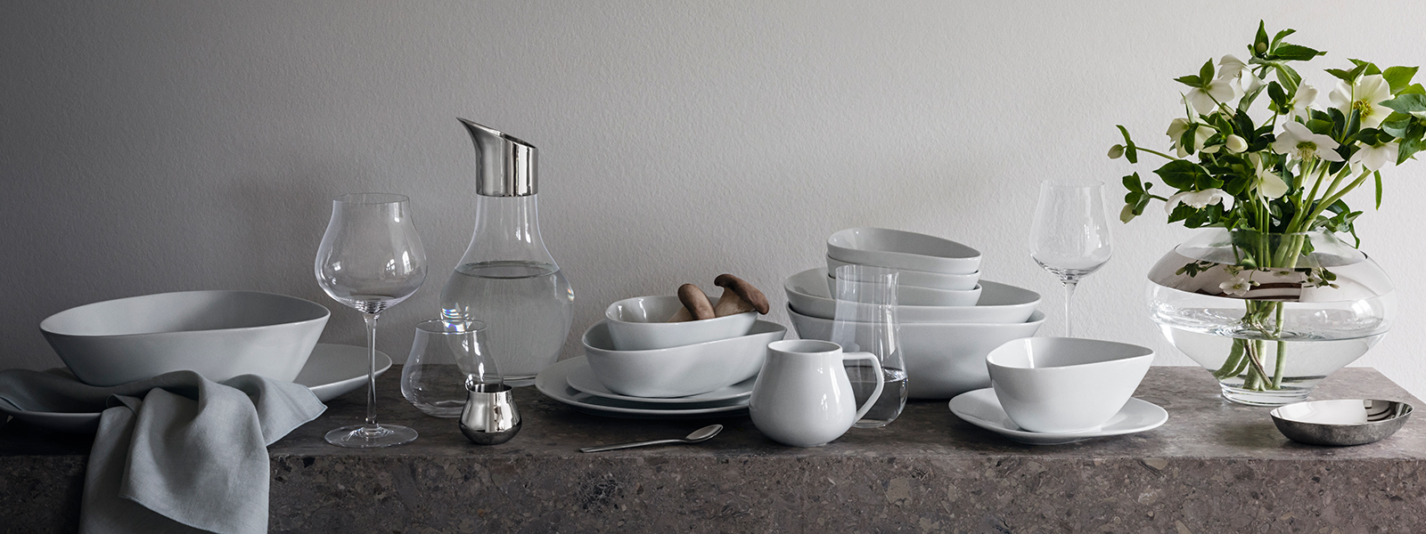 Indoor tablesetting featuring porcelain plates and bowls together with crystal clear glasses and mirror polished stainless steel vase from the Sky collection