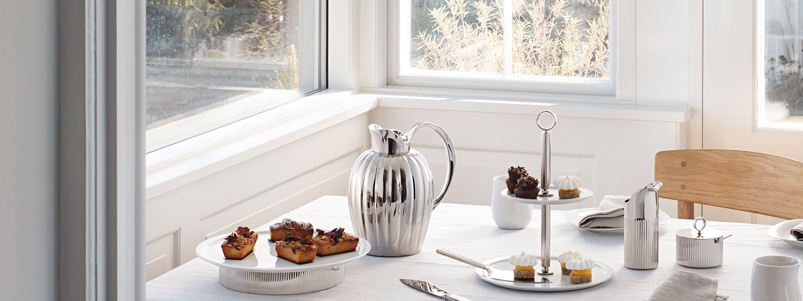 Still life image of mirror polished stainless steel pitcher, kicthen roll holder and cake knife from the Bernadotte collection
