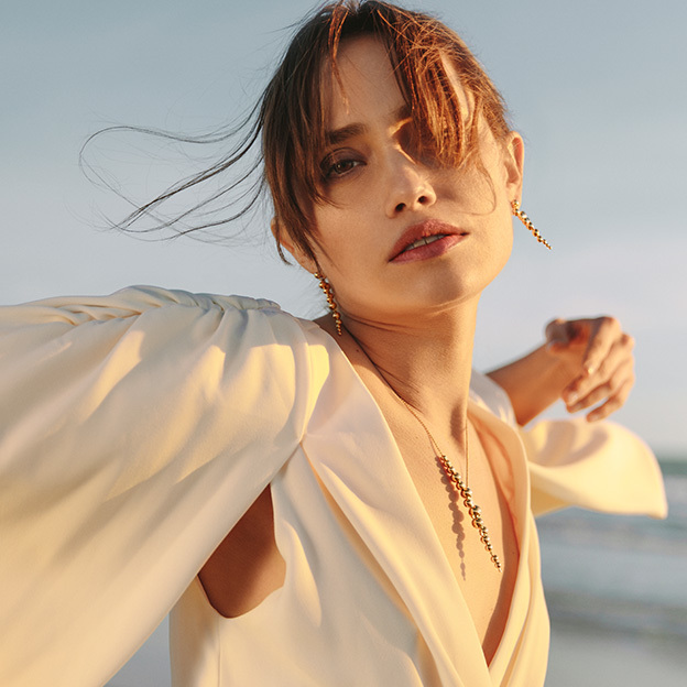 necklace and long grape earrings in 18 kt. yellow gold with white diamonds from the moonlight grapes range on model at the beach by georg jensen jewellery
